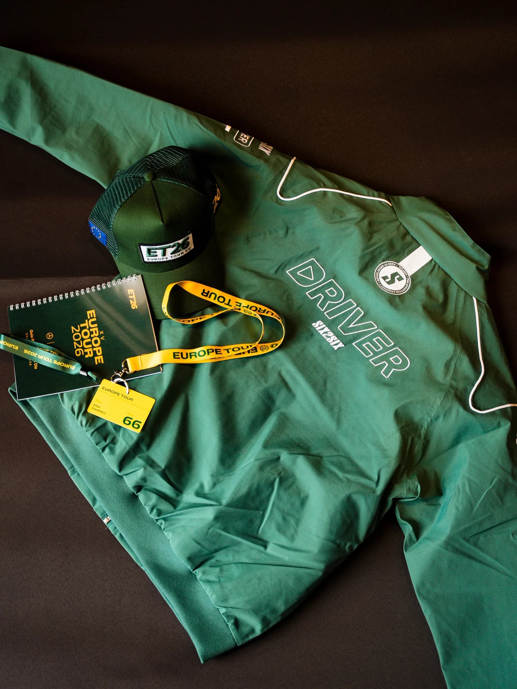 The SIX2SIX Driver jacket and ET26 cap laid flat beside the tour lanyard, credential and roadbook