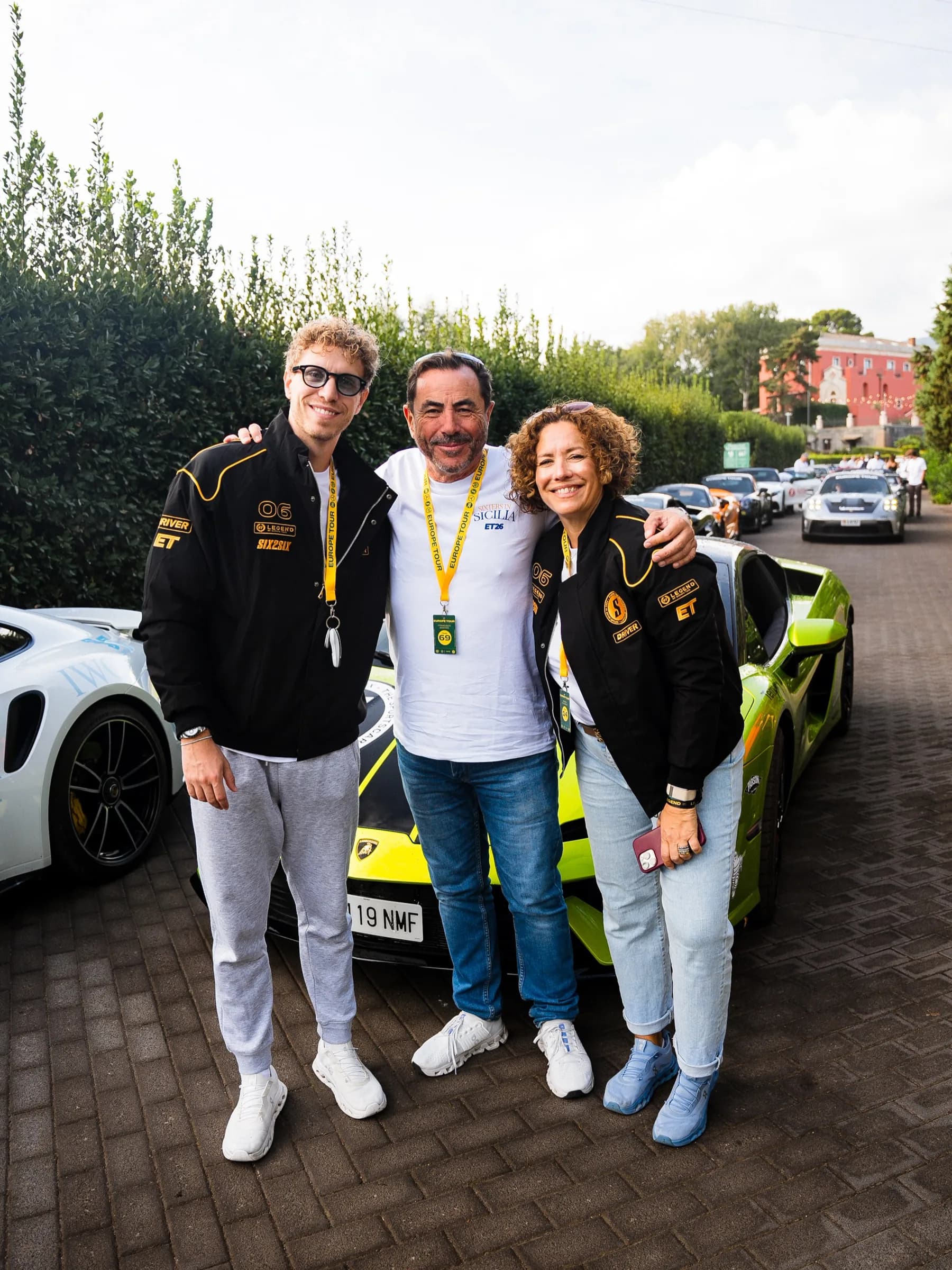 Three SIX2SIX drivers, two in the black and yellow Legend jacket, with supercars lined up behind them