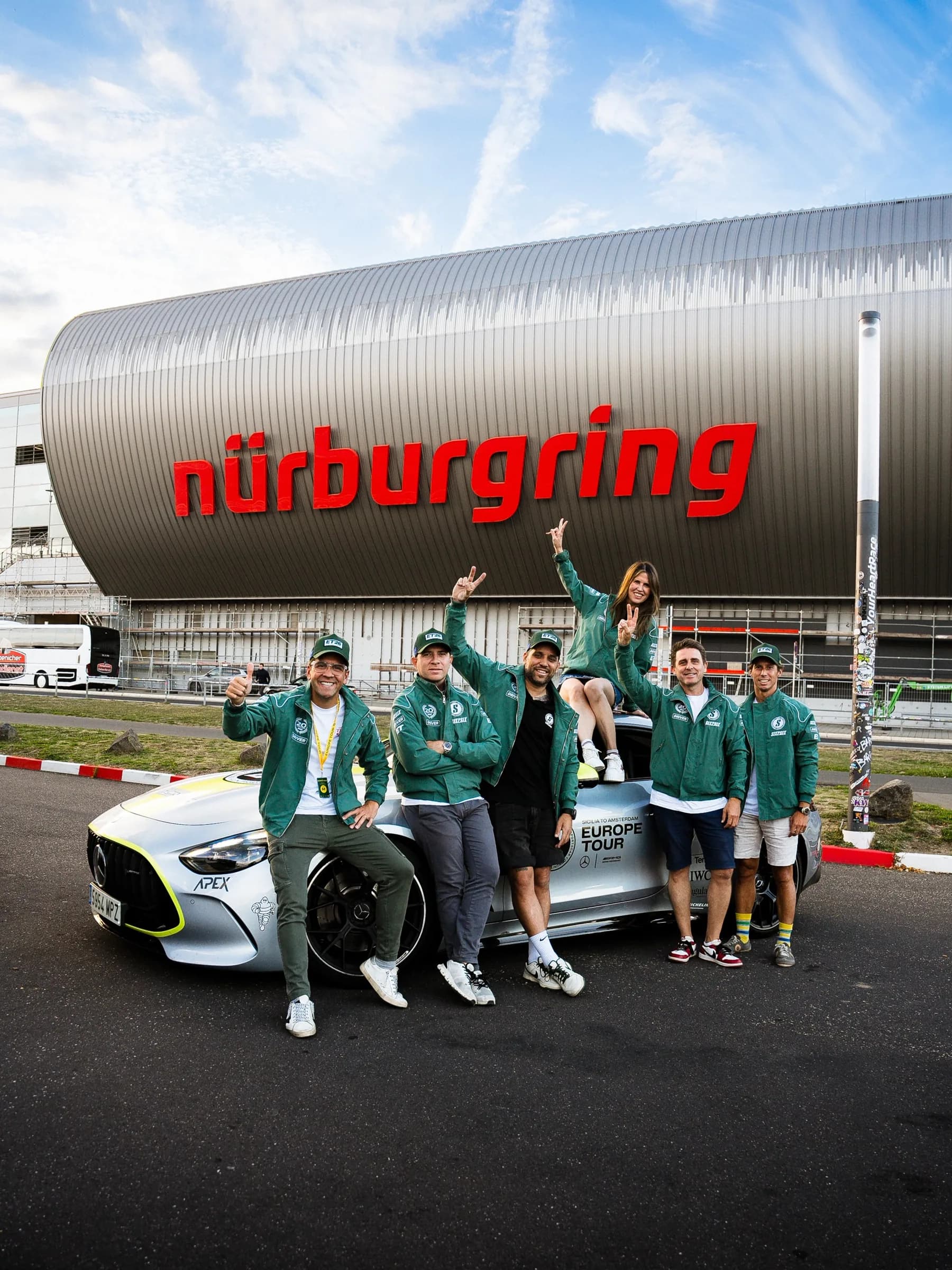 Six SIX2SIX drivers in Driver jackets and ET26 caps on a silver Mercedes-AMG in front of the Nürburgring
